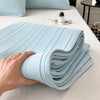 A hand is folding a light blue cooling ice silk bed pad on a white table.