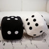 A black and white polka dot plush dice throw pillow resting on a white sofa.