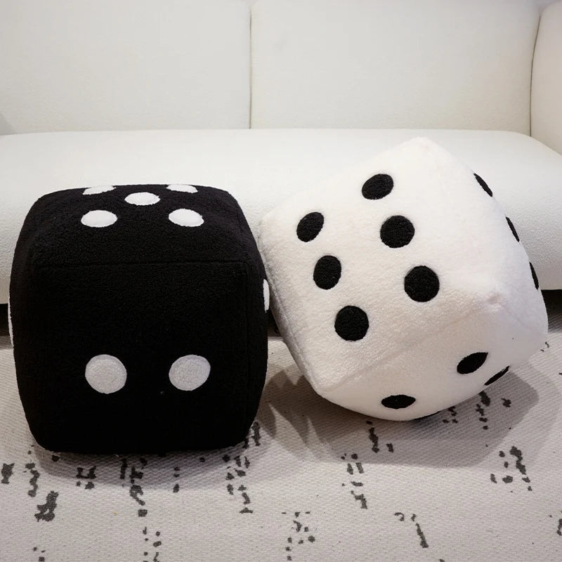 A black and white polka dot plush dice throw pillow resting on a white sofa.