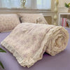 A rolled light pink quilt blanket with a floral print is displayed on a purple surface.