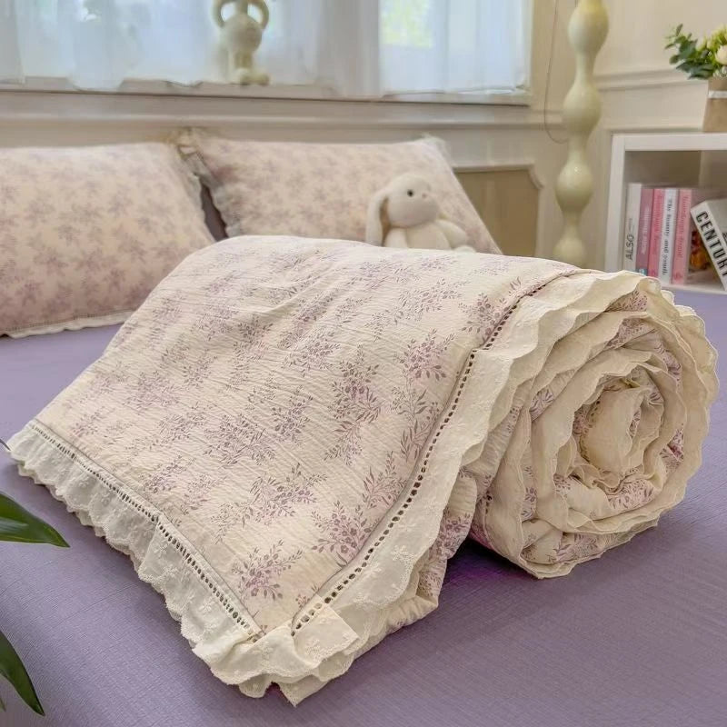 A rolled light pink quilt blanket with a floral print is displayed on a purple surface.