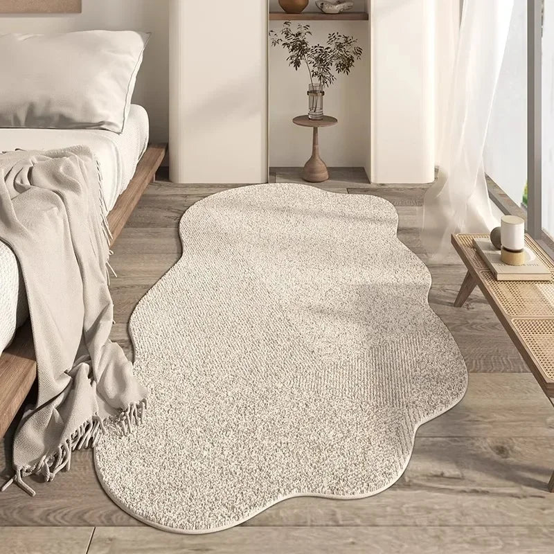 A light beige irregular plush area rug placed on a wooden floor in a bright room.