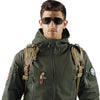 A man wearing a dark olive green tactical jacket with embroidered patches and sunglasses.