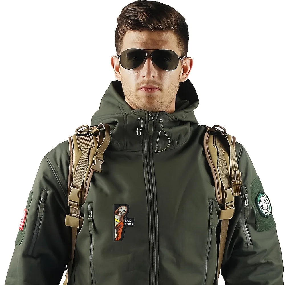 A man wearing a dark olive green tactical jacket with embroidered patches and sunglasses.