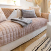 A beige velvet sofa protection cover with quilted cushions and a matching throw blanket on a light wood floor.