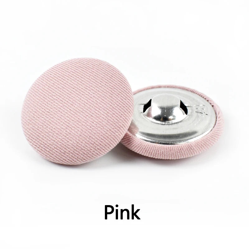 A pink round fabric-covered shank button is shown next to its silver metal base.