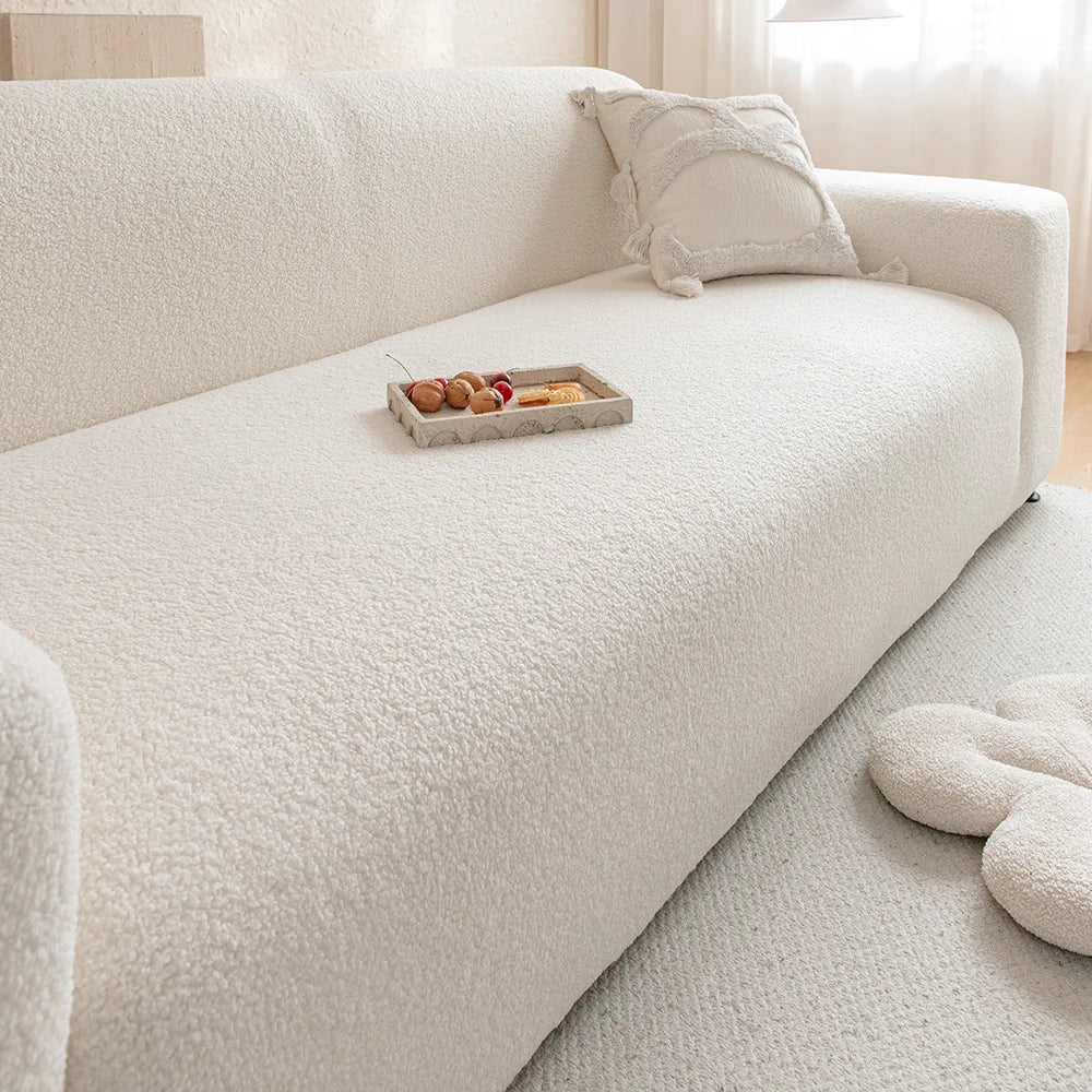 A white Jacquard velvet sofa cover with a light beige throw pillow and a wooden tray of fruit on the seat.
