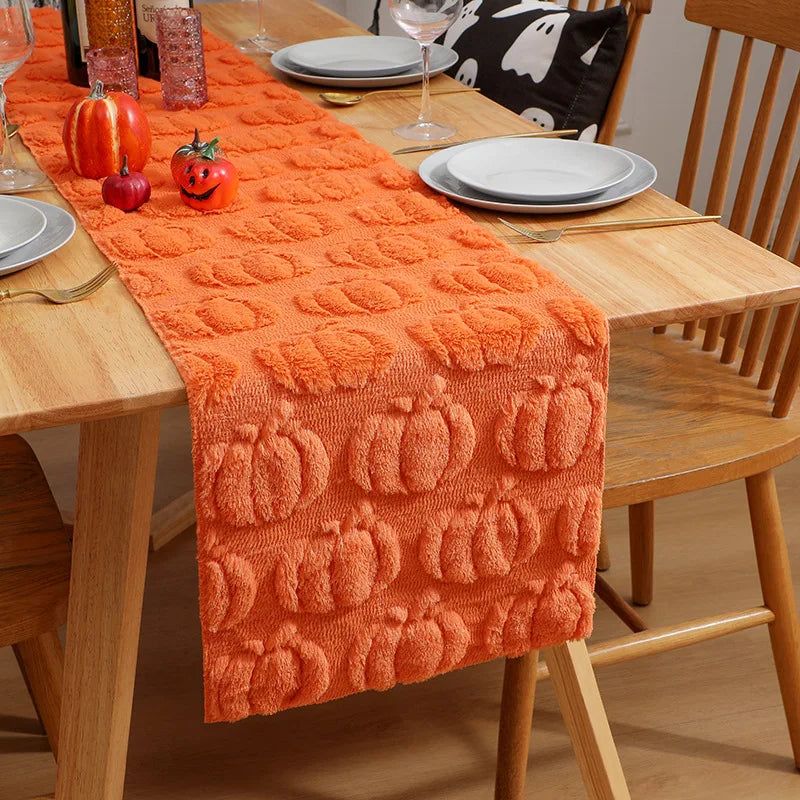 An orange knitted table runner with pumpkin patterns placed on a wooden dining table.