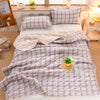 A plaid quilt set featuring light gray and white tones displayed on a bed with pillows and a throw blanket.