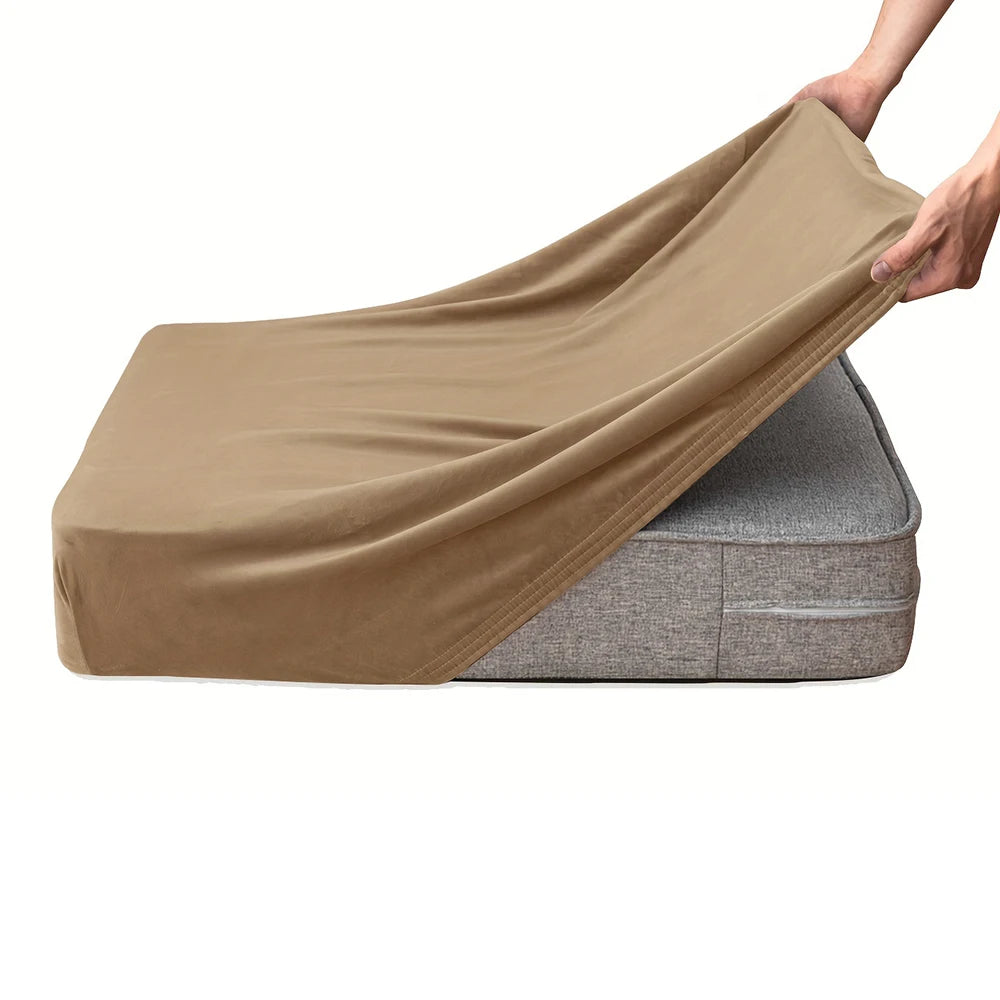 A hand is draping a beige velvet stretchy sofa seat cover over a gray cushion.